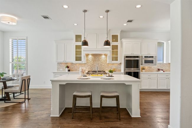 Kitchen with double oven, a center island with sink, white cabinets, a kitchen bar, and decorative backsplash | Image 6