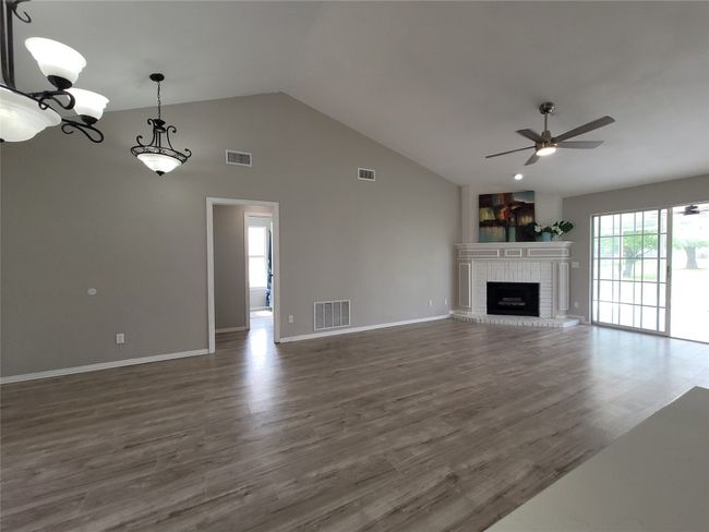 Vaulted ceiling with modern light fixtures featuring a ceiling fan, dark wood-style flooring, and a brick fireplace | Image 5