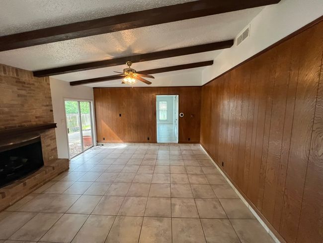 Unfurnished living room with wood walls, a textured ceiling, beamed ceiling, a ceiling fan, and light tile patterned floors | Image 4