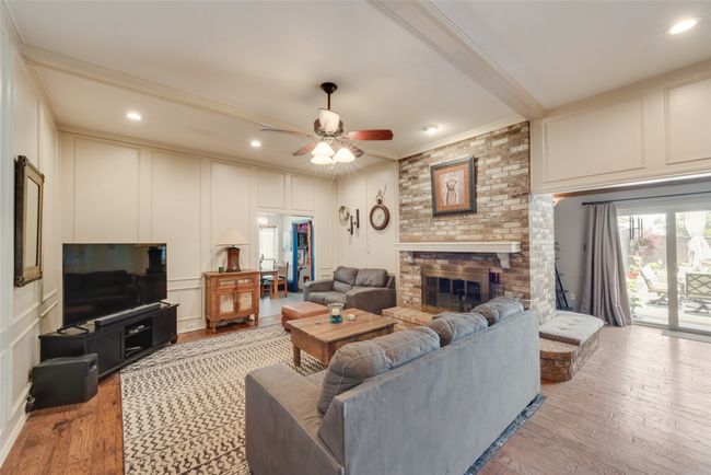 Living room with a decorative wall, ornamental molding, ceiling fan, light wood finished floors, and a fireplace | Image 7