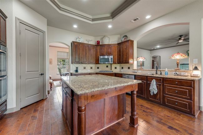 Kitchen featuring arched walkways, stainless steel microwave, a tray ceiling, a ceiling fan, and recessed lighting | Image 20