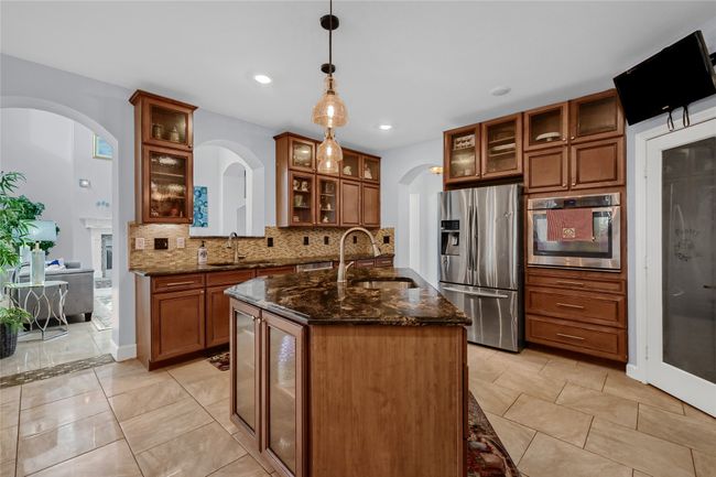 Kitchen featuring dark stone counters, sink, hanging light fixtures, decorative backsplash, and appliances with stainless steel finishes | Image 15