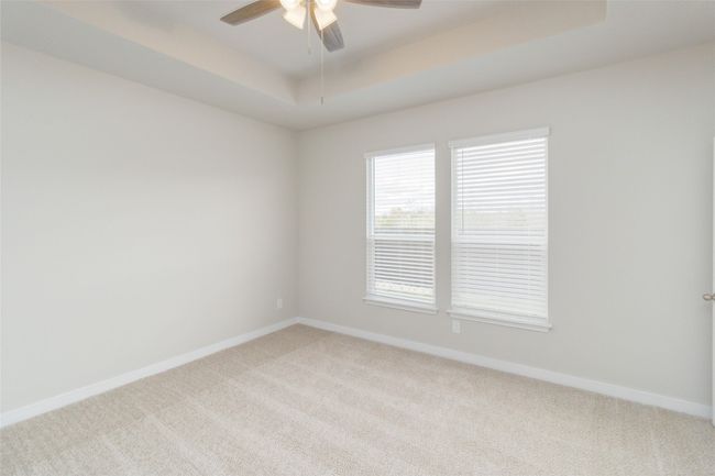 Empty room featuring a tray ceiling, light carpet, ceiling fan, and baseboards | Image 28