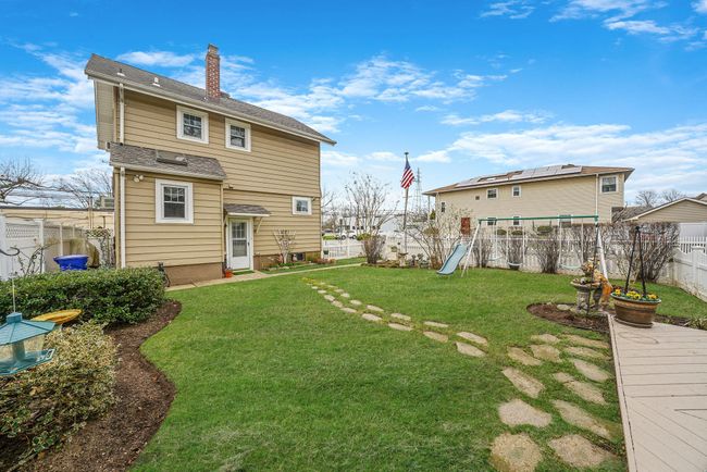 Back of house featuring a chimney, a fenced backyard, a shingled roof, a lawn, and a playground | Image 24