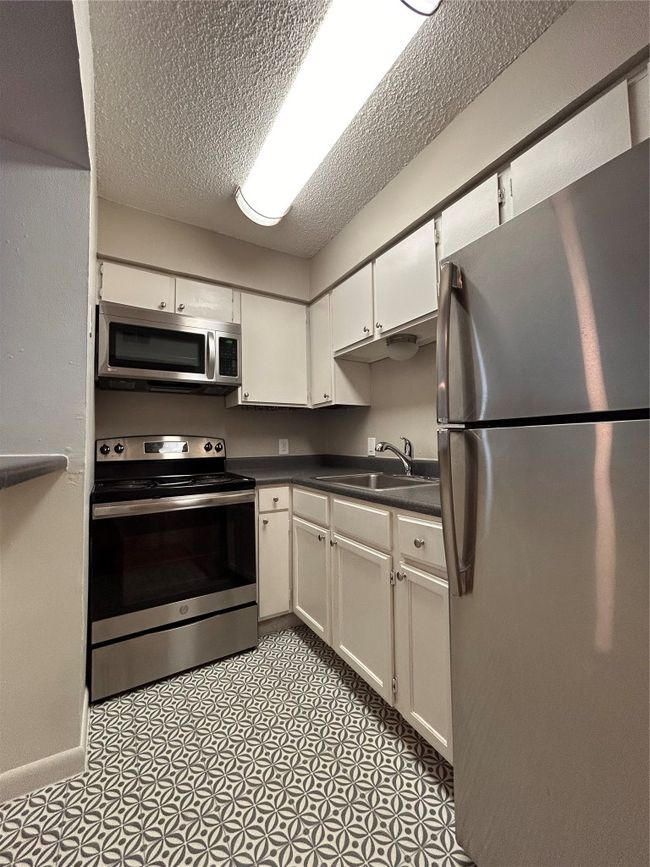Kitchen with appliances with stainless steel finishes, dark countertops, a textured ceiling, and white cabinets | Image 4