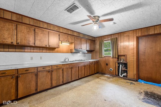 Kitchen featuring brown cabinetry, light countertops, ceiling fan, and wooden walls | Image 24