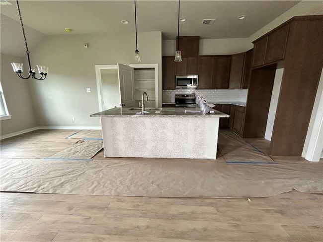 Kitchen featuring appliances with stainless steel finishes, light stone countertops, an island with sink, tasteful backsplash, and dark brown cabinets | Image 6