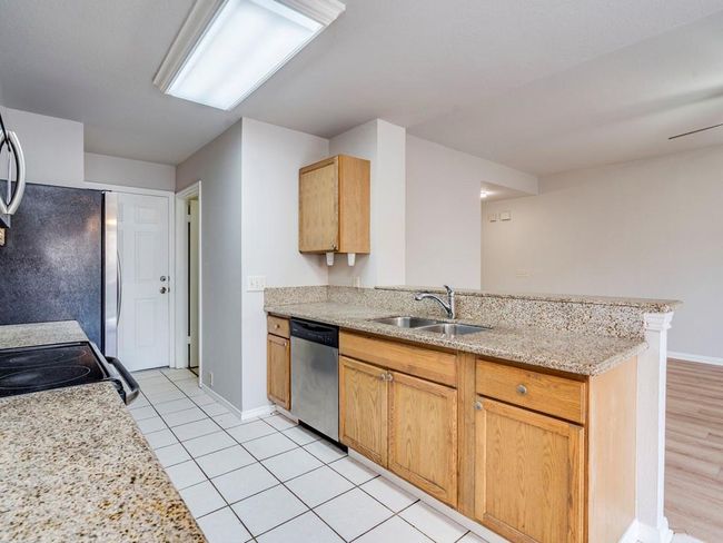Kitchen featuring a peninsula, stainless steel dishwasher, light tile patterned floors, light stone counters, and electric stove | Image 14