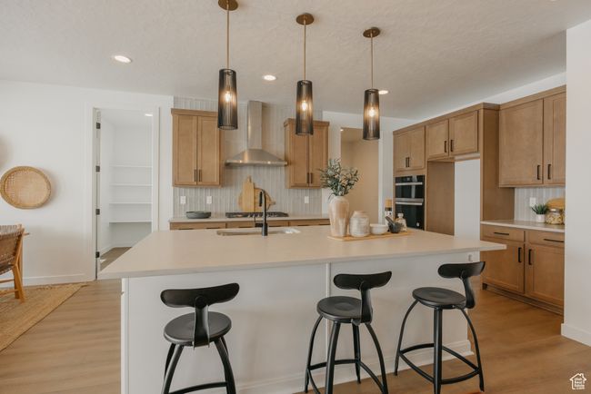 Kitchen featuring wall chimney range hood, backsplash, a sink, a kitchen bar, and recessed lighting | Image 22