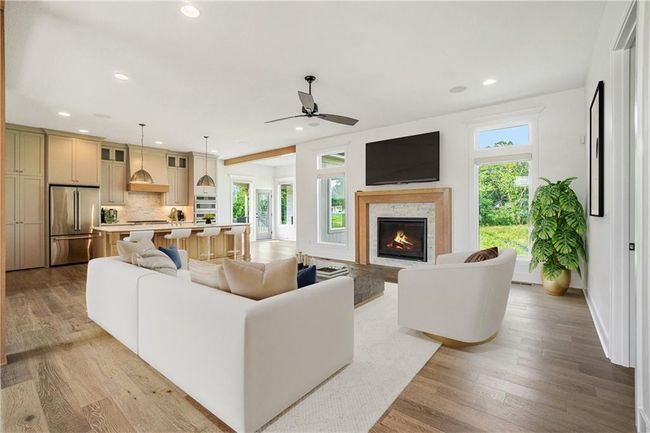 Living room with a warm lit fireplace, recessed lighting, light wood finished floors, a ceiling fan, and baseboards | Image 9