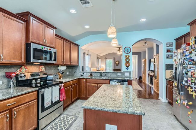 Kitchen featuring a center island, a sink, arched walkways, visible vents, and appliances with stainless steel finishes | Image 12