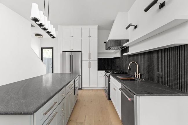 Kitchen with appliances with stainless steel finishes, white cabinets, light wood-type flooring, tasteful backsplash, and dark stone countertops | Image 10