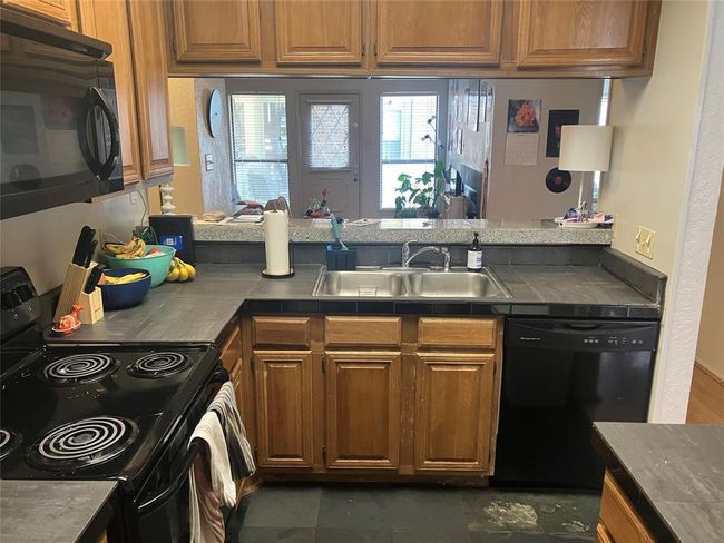 Kitchen with black appliances, a sink, a peninsula, brown cabinets, and tile counters | Image 8