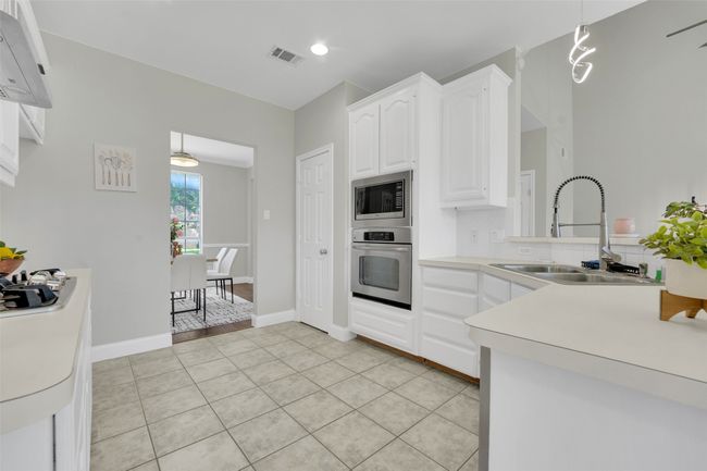 Kitchen featuring appliances with stainless steel finishes, white cabinets, light tile patterned floors, light countertops, and hanging light fixtures | Image 10