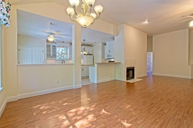 Unfurnished living room with ceiling fan, a chandelier, light wood-style flooring, and a tiled fireplace | Image 12