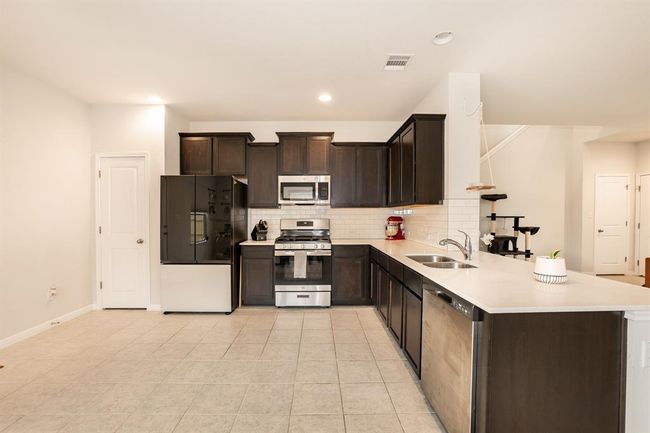 Kitchen with stainless steel appliances, tasteful backsplash, dark brown cabinets, light countertops, and a peninsula | Image 15