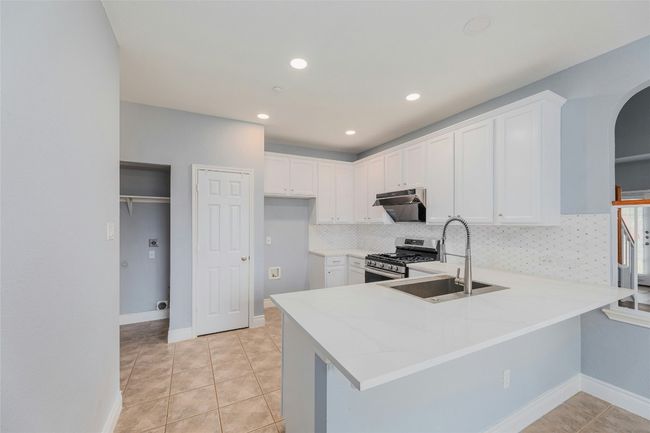 Kitchen with gas range, exhaust hood, arched walkways, a peninsula, and tasteful backsplash | Image 12