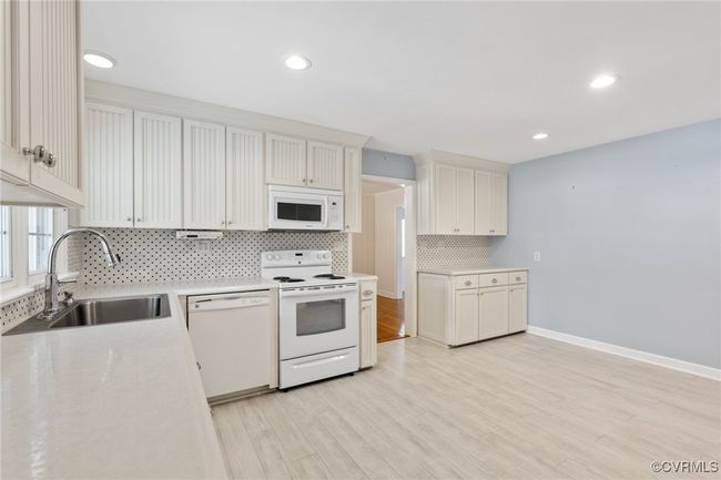 Kitchen featuring white appliances, decorative backsplash, light countertops, a sink, and light wood-type flooring | Image 15