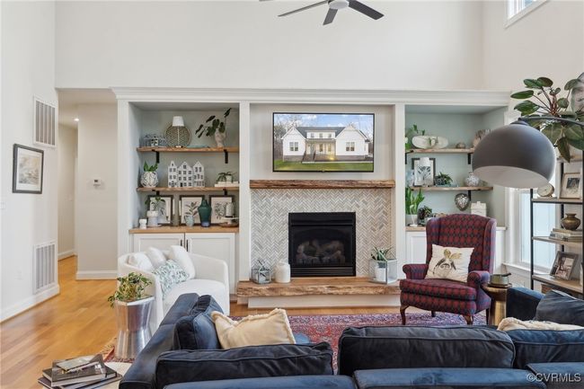 Living room with visible vents, ceiling fan, a tiled fireplace, light wood-type flooring, and a towering ceiling | Image 4