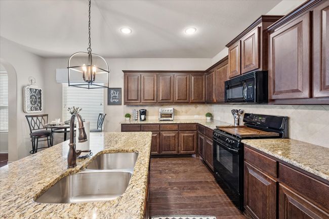 Kitchen with a chandelier, black appliances, dark wood-type flooring, arched walkways, and a sink | Image 13