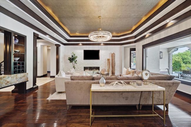 This welcoming living room is perfectly tailored for entertaining. From this vantage point, the imported Onyx serving bar—ideally positioned between the living and formal dining rooms—offers easy access for serving cocktails during gatherings. The open-concept layout encourages effortless flow into surrounding spaces, while the expansive picture windows highlight the covered patio and lush landscape, beautifully merging indoor comfort with outdoor charm. | Image 15