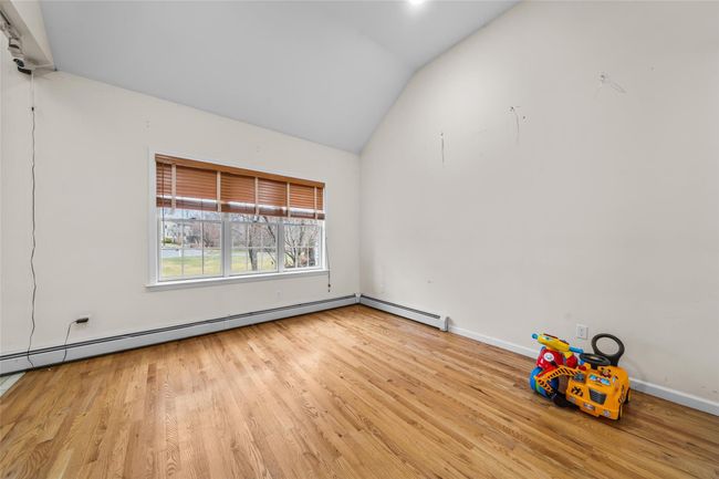 Unfurnished room featuring a baseboard radiator, wood finished floors, vaulted ceiling, and baseboards | Image 6