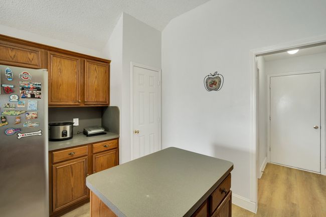 Kitchen featuring freestanding refrigerator, light wood-style floors, vaulted ceiling, brown cabinets, and a kitchen island | Image 16