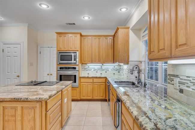 Kitchen with appliances with stainless steel finishes, light stone counters, crown molding, tasteful backsplash, and a kitchen island | Image 20