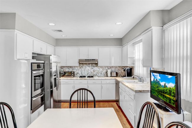 Kitchen featuring stainless steel appliances, white cabinetry, sink, and backsplash | Image 14
