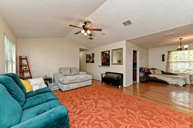 Living area featuring a textured ceiling, wood finished floors, a ceiling fan, and vaulted ceiling | Image 6