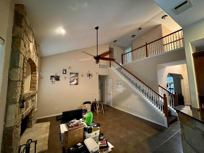 Unfurnished living room with ceiling fan, high vaulted ceiling, a stone fireplace, and stairs | Image 7