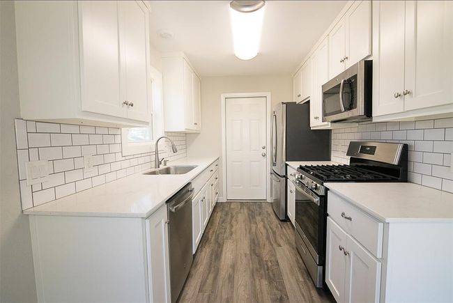 Kitchen featuring appliances with stainless steel finishes, dark wood-style flooring, white cabinets, and backsplash | Image 6