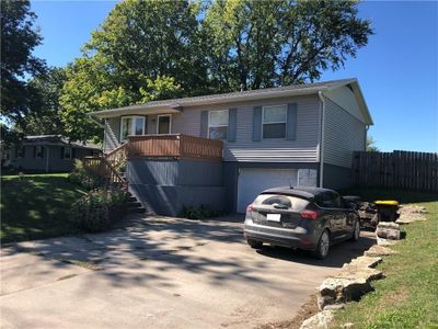 View of front of home with a wooden deck, a front yard, and a garage | Image 1