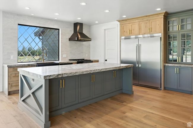 Kitchen featuring wall chimney exhaust hood, built in fridge, backsplash, light wood-style flooring, and a kitchen island | Image 18