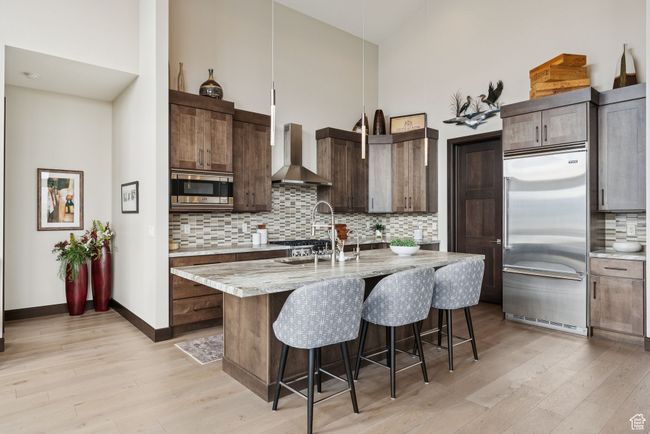 Kitchen featuring built in appliances, wall chimney exhaust hood, high vaulted ceiling, light wood-style flooring, and decorative backsplash | Image 21