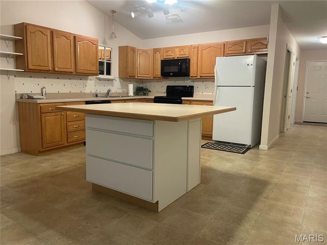Kitchen featuring black appliances, vaulted ceiling, open shelves, light countertops, and a kitchen island | Image 5