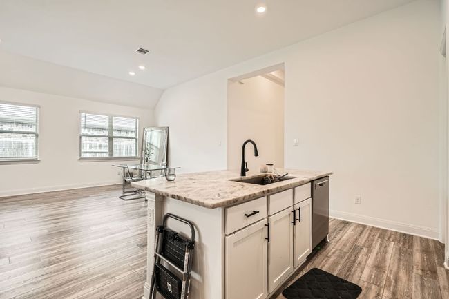 Kitchen with light wood-style flooring, stainless steel dishwasher, an island with sink, light stone countertops, and vaulted ceiling | Image 12