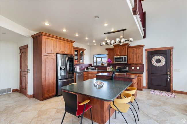 Kitchen with dark countertops, tasteful backsplash, an island with sink, appliances with stainless steel finishes, and visible vents | Image 6