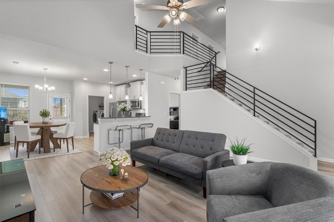Living area featuring a chandelier, light wood-style floors, stairway, a ceiling fan, and a high ceiling | Image 7