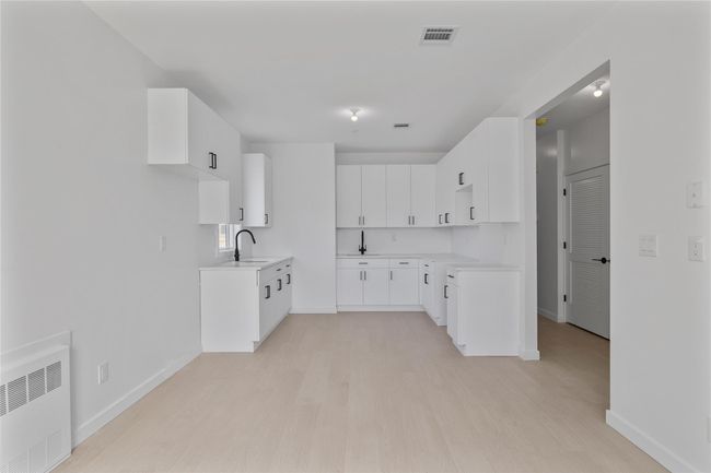 Kitchen with radiator heating unit, light wood finished floors, a sink, and visible vents | Image 41