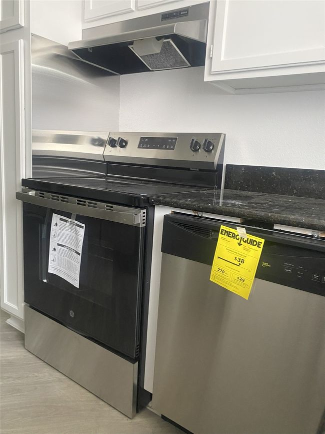 Kitchen with ventilation hood, appliances with stainless steel finishes, white cabinets, dark stone countertops, and wood finished floors | Image 8