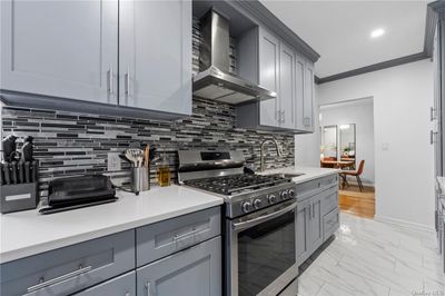 Kitchen with backsplash, crown molding, wall chimney exhaust hood, stainless steel range with gas cooktop, and sink | Image 1