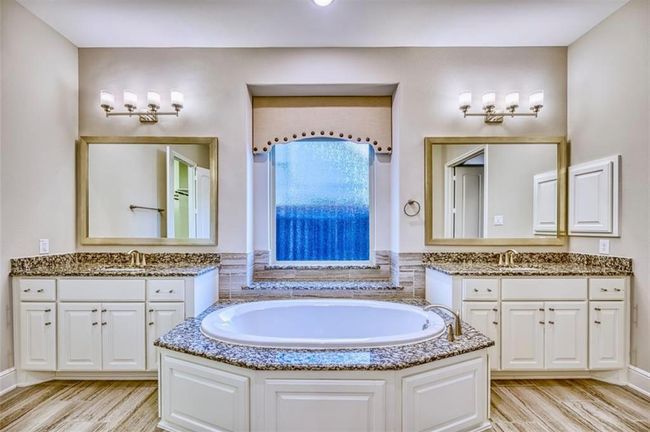 This bathroom features a luxurious central bathtub with granite countertops, dual vanities with large mirrors, and elegant lighting fixtures, creating a spa-like atmosphere. | Image 30