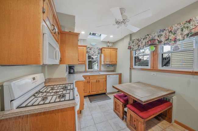 Kitchen featuring light countertops, a skylight, white appliances, a ceiling fan, and a sink | Image 11