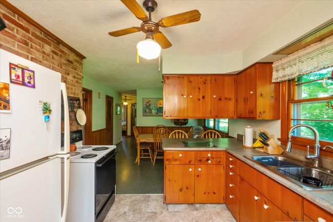 kitchen with white appliances, a textured ceiling, a ceiling fan, brown cabinets, and a peninsula | Image 12