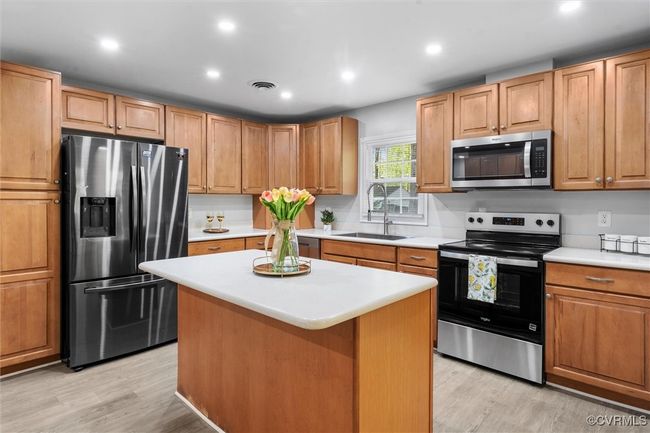 Kitchen with appliances with stainless steel finishes, light countertops, light wood-type flooring, a sink, and visible vents | Image 9