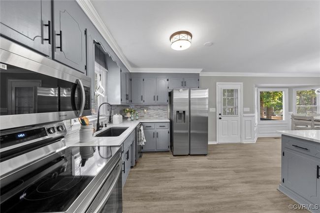 Kitchen featuring gray cabinets, stainless steel appliances, ornamental molding, light countertops, and light wood-style floors | Image 18
