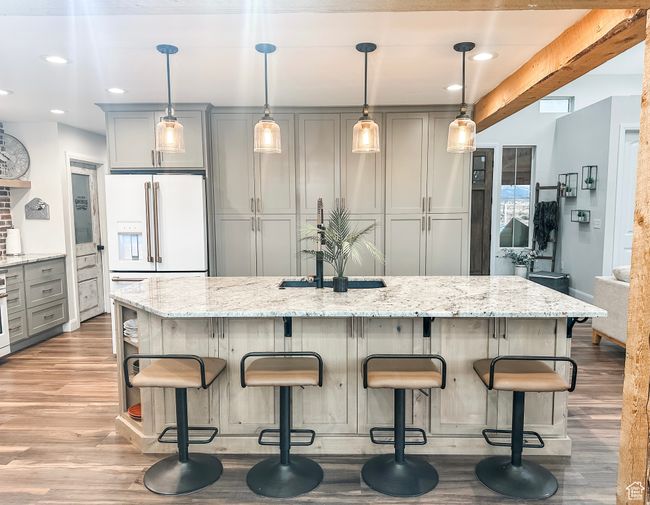 Kitchen featuring light stone counters, white refrigerator with ice dispenser, a breakfast bar area, wood finished floors, and gray cabinetry | Image 9
