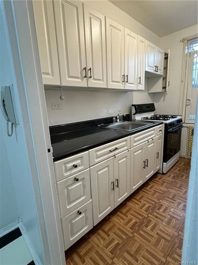 Kitchen featuring sink, stove, dark parquet flooring, and white cabinetry | Image 3