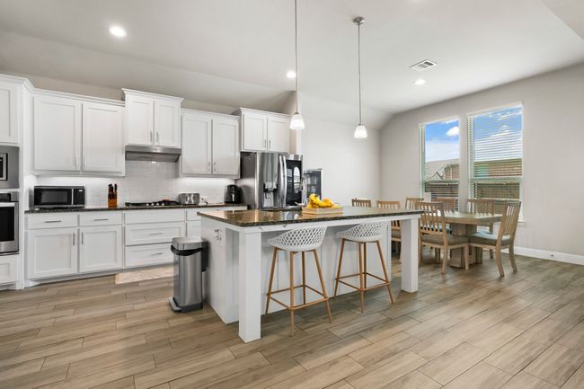 Kitchen featuring backsplash, a center island, a kitchen breakfast bar, light wood-style floors, and white cabinets | Image 8